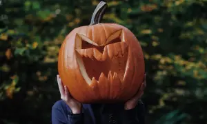 Przerażająca dynia halloween szablon z wyciętymi zębami i oczami, trzymana przed twarzą.