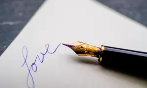Eleganckie pióro wieczne pisze słowo "love" fioletowym atramentem na białej kartce.