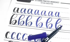 Ćwiczenie kaligrafii litery "a" i "b" na arkuszu Tombow. Niebieski pisak i jego nakrętka leżą obok.