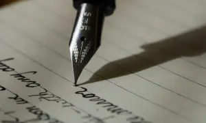 Stalówka pióra wiecznego kreśli słowa na papierze w linie. Dzień pisma ręcznego celebruje piękno odręcznych notatek.