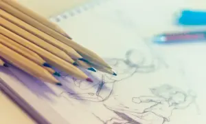 Kolorowe kredki leżą na szkicowniku, gdzie trwa nauka rysowania postaci w ruchu.