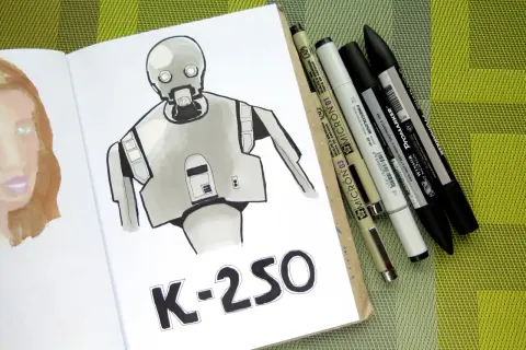 Rysunki markerami przedstawiają robota K-2SO i fragment twarzy. Obok leżą różnorodne pisaki.