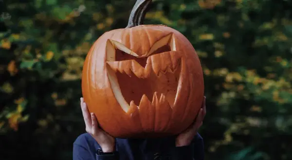 Przerażająca dynia halloween szablon z wyciętymi zębami i oczami, trzymana przed twarzą.