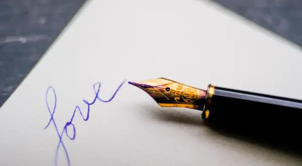 Eleganckie pióro wieczne pisze słowo "love" fioletowym atramentem na białej kartce.