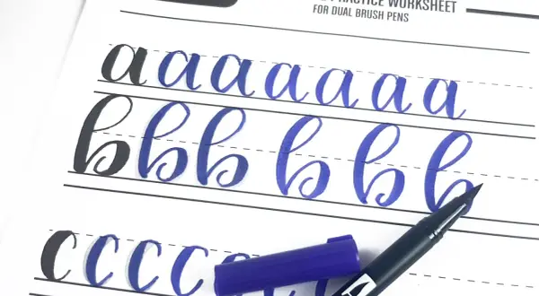 Ćwiczenie kaligrafii litery "a" i "b" na arkuszu Tombow. Niebieski pisak i jego nakrętka leżą obok.