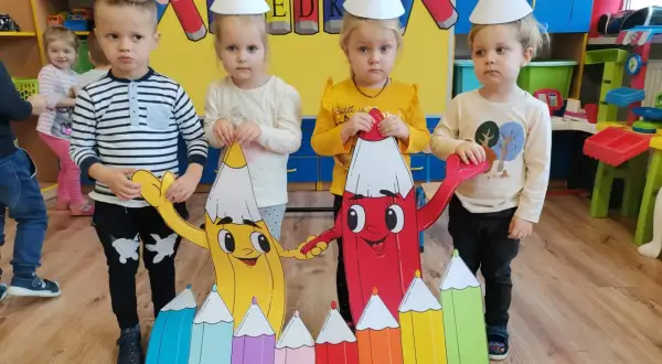 Dzieci w czapkach świętują Dzień Kredki, trzymając kolorowe postacie.