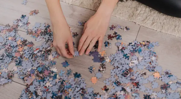 Ręce układają fragmenty obrazka, tworząc własne dzieło sztuki. To relaksujące puzzle DIY.