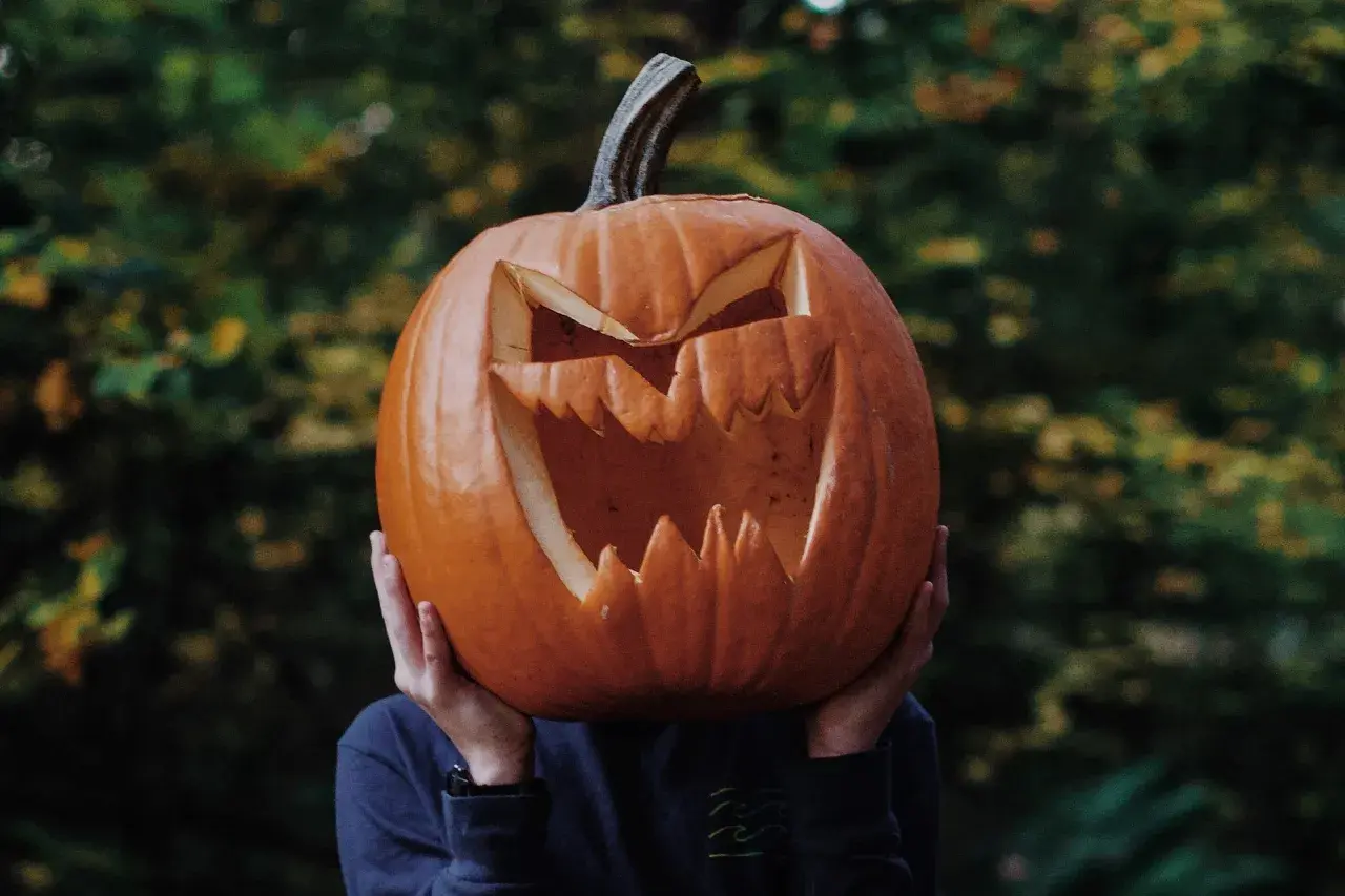 Przerażająca dynia halloween szablon z wyciętymi zębami i oczami, trzymana przed twarzą.