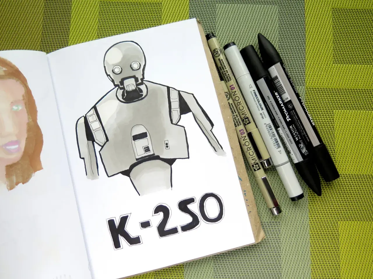 Rysunki markerami przedstawiają robota K-2SO i fragment twarzy. Obok leżą różnorodne pisaki.
