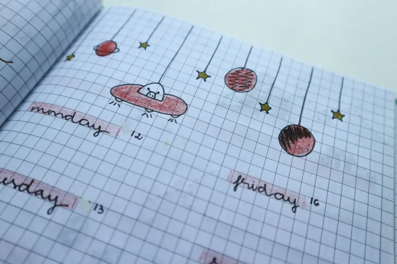 Kosmiczne bullet journal pomysły: latający spodek, planety i gwiazdy na kratkowanym papierze.