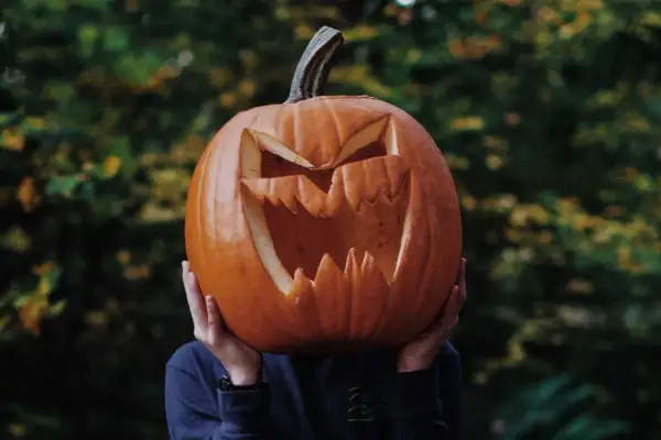 Przerażająca dynia halloween szablon z wyciętymi zębami i oczami, trzymana przed twarzą.